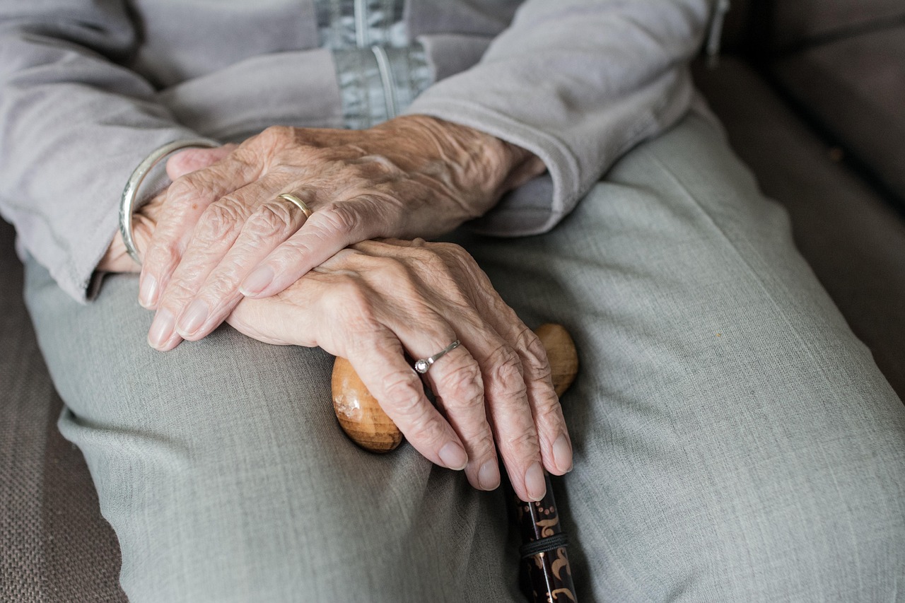 An elderly person's hands resting on a cane